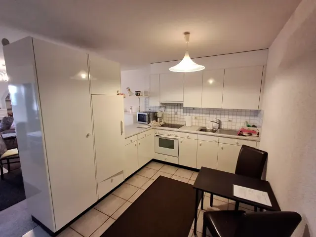 BookNoFees holiday home in Gailingen, Baden-Württemberg, Germany – Kitchen with white cabinets, stove, sink, microwave, and small dining table with chairs