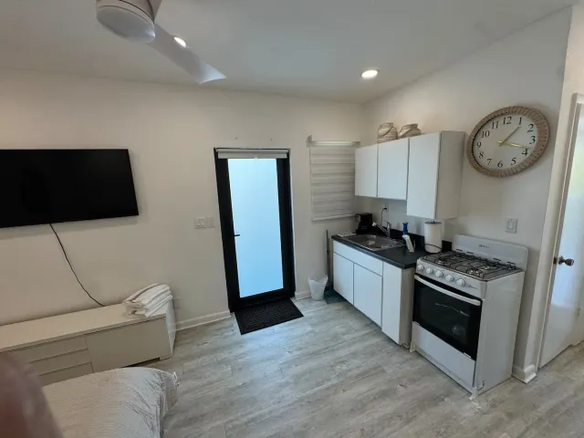 BookNoFees holiday home in Cutler Bay, United States – Studio kitchen with white cabinets, gas stove, wall clock, and glass door