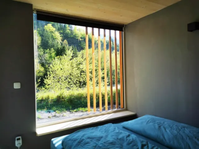 BookNoFees holiday home in Hieflau, Styria, Austria – Bedroom with blue bedding and large window with wooden slats overlooking forest