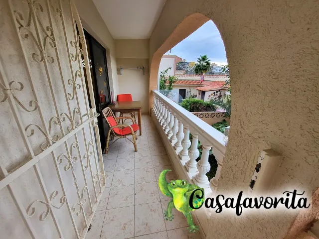 BookNoFees holiday home in Buen Paso, Tenerife, Spain – Balcony with table, red chairs, and view of rooftops and palm trees