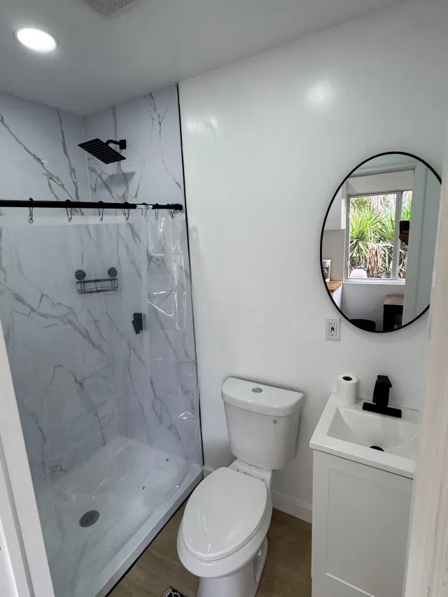 BookNoFees holiday home in Cutler Bay, United States – Bathroom with marble-patterned shower, toilet, sink, and round mirror