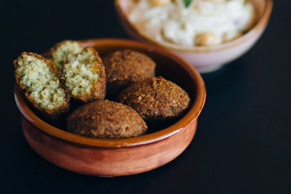 BookNoFees: Example photo: Falafel balls, including a cut-open piece, in a bowl with hummus behind